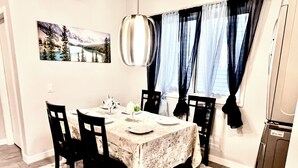 A dining area with a table set for four, chairs, a rug, a painting on the wall, and a hanging light fixture. - Bungalow | Upper Level | CT Train | Spruce Meadow (Calgary)