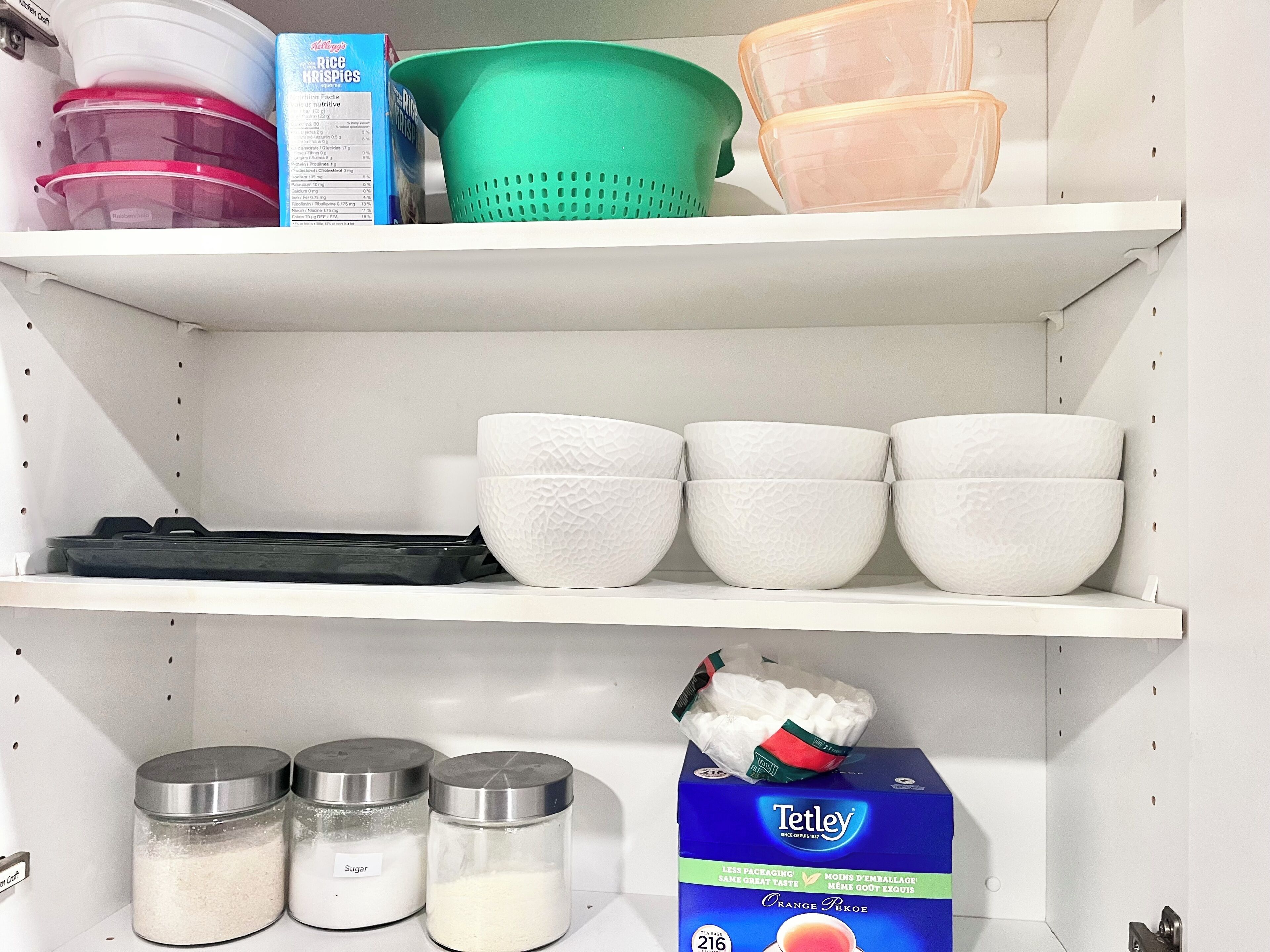 A kitchen shelf with storage containers, a box of sugar, and a box of orange pekoe tea.