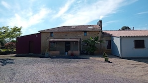Una casa de dos pisos con techo de tejas, camino de entrada de grava y un pequeño jardín con plantas en macetas.
