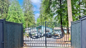 A gated property with a metal gate featuring animal cutouts, a blue building, and a forested background. - A Cozy HomeAway Home @Bridle Trail, Bellevue, WA (Bellevue)