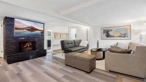 A modern living room with a fireplace, a grey sofa, a beige sofa, and a flat-screen TV mounted on a stone wall. - A Cozy HomeAway Home @Bridle Trail, Bellevue, WA (Bellevue)