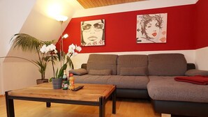 Ein Wohnzimmer mit einer Couch, einem Couchtisch und einer Lampe. An der Wand hängen zwei Gemälde und auf dem Boden steht eine Pflanze.