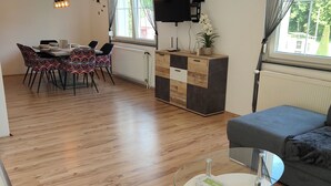 A modern living room with a dining area, a flat-screen TV mounted on the wall, and a sofa. - Spacious, newly renovated apartment in southern Burgenland with its own balcony! (Oberdrosen)