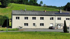 A two-story building with a flat roof and solar panels, surrounded by a green field and trees. - Spacious, newly renovated apartment in southern Burgenland with its own balcony! (Oberdrosen)