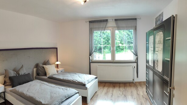 A bedroom with two beds, a window with curtains, a radiator, and a refrigerator. - Spacious, newly renovated apartment in southern Burgenland with its own balcony! (Oberdrosen)