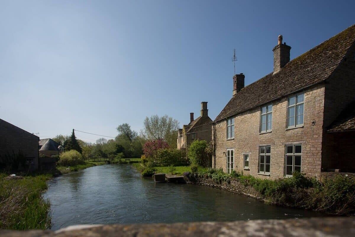 A narrow waterway flanked by stone buildings with chimneys, a lock, and lush greenery.
