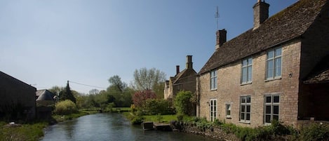 A narrow waterway flanked by stone buildings with chimneys, a lock, and lush greenery.