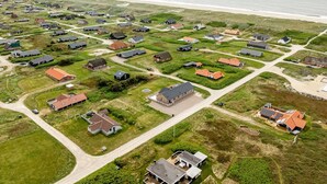 Luchtbeeld van een kustgebied met woonhuizen, wegen en windturbines op de achtergrond.