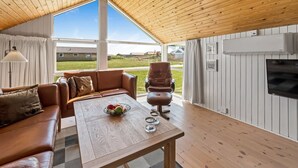 Een knus ingerichte kamer met een houten plafond, een leren bank, een eettafel met fruit en een televisie.