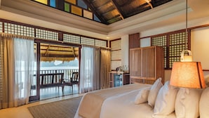 A hotel room with a large bed, a desk, a chair, and a view of the sea through a glass door. - Mua Tala Hotel (El Nido)