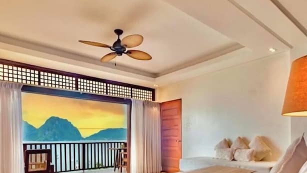 A bedroom with a bed, a ceiling fan, a view of mountains, and a balcony. - Mua Tala Hotel (El Nido)