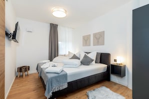 A modern bedroom with a bed, bedside tables, a wall-mounted TV, and artwork. - MyWinkl8 - Alpenwinkl (Reit im Winkl)