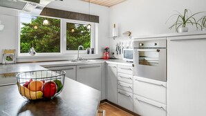 Een moderne keuken met witte kastjes, een groot raam en een schaal fruit op het aanrecht.