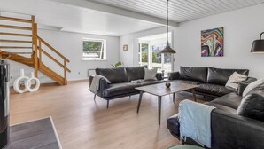 En rummelig opholdsstue med en trætrappe, lædersofaer, et sofabord og et loft med synlige bjælker.