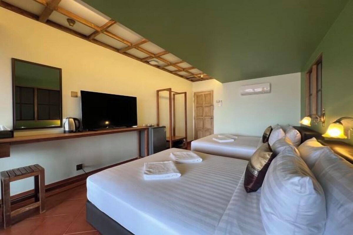 A hotel room with a bed, a television, a desk with a computer, and a small stool.