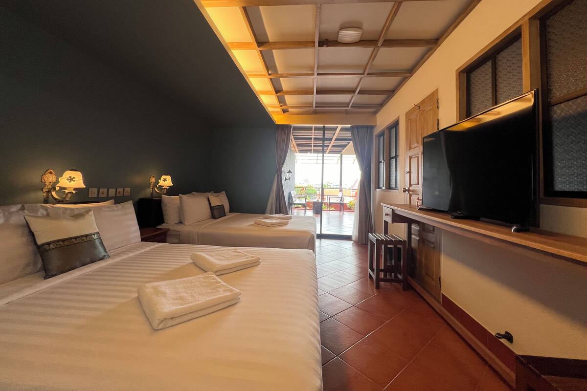 A hotel room with two beds, a TV, a desk, and a view of the outside.