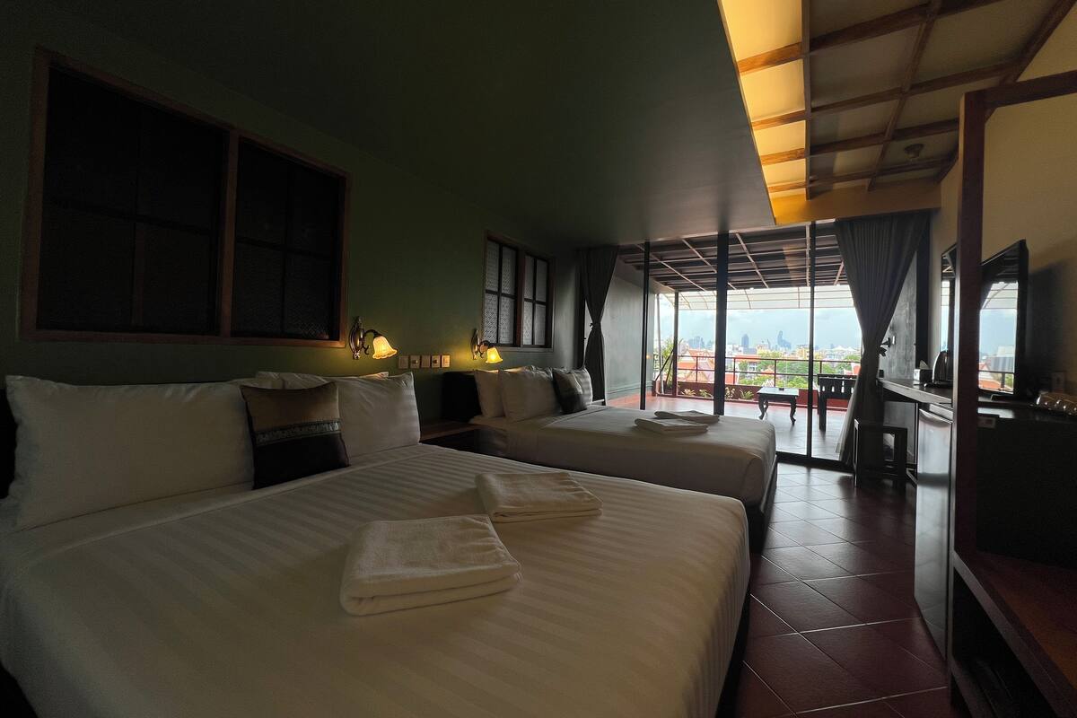 A hotel room with two beds, a balcony, and a city view.