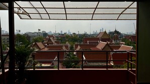 A view from a balcony with traditional Thai architecture, a city skyline in the background, and a metal roof structure. - Cha Na Stay at Merry V (Bangkok)