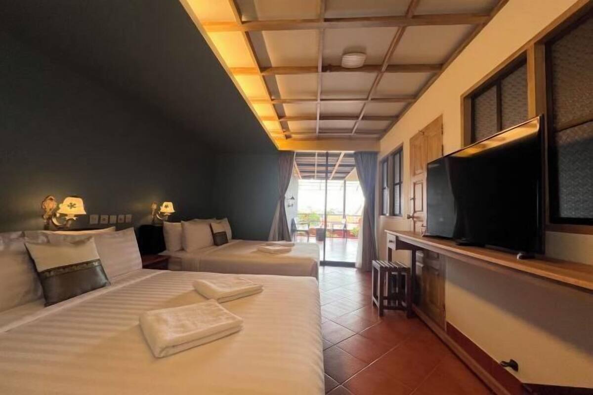 A hotel room with two beds, a TV, and a view of the outdoors.