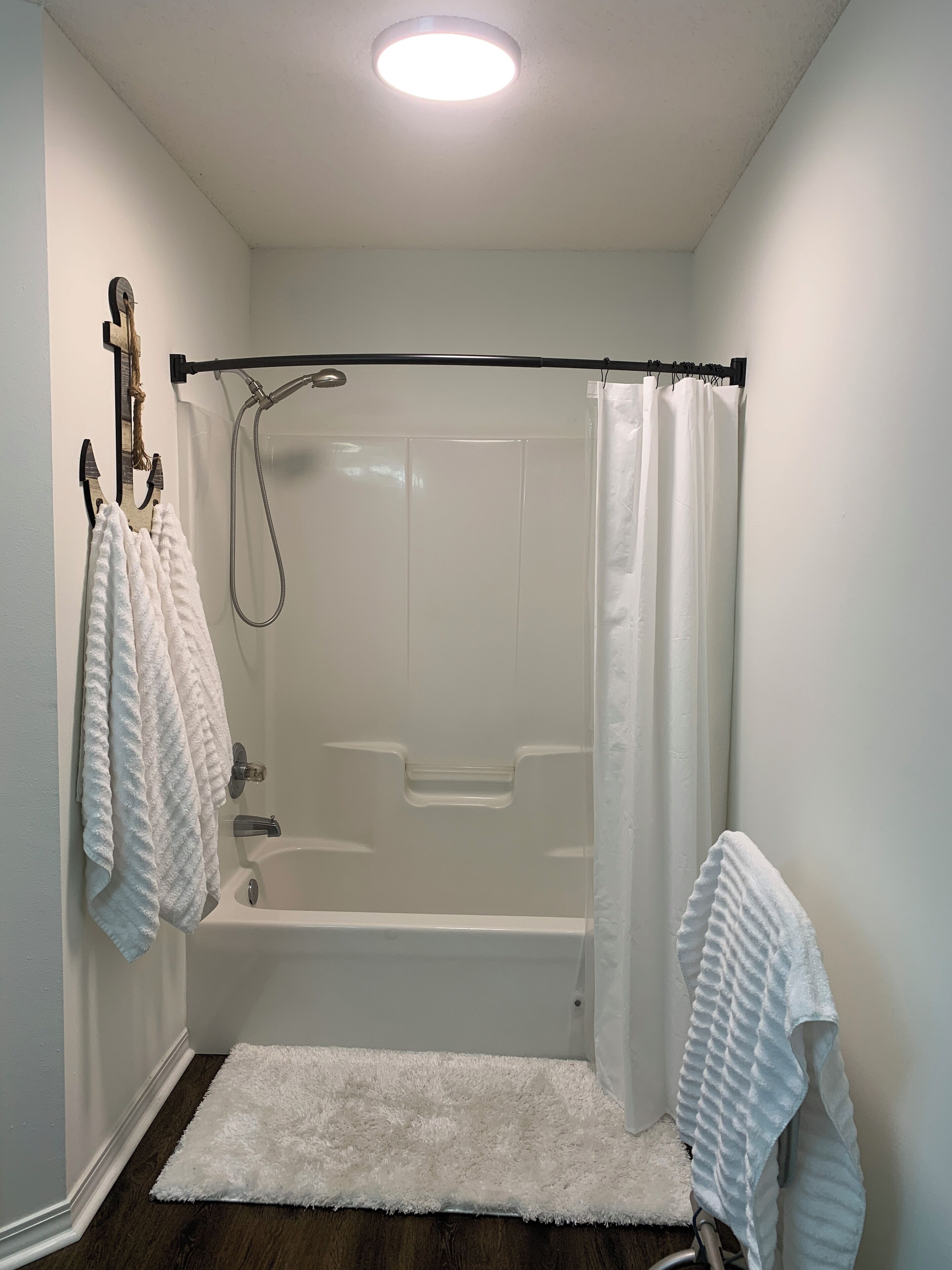 Une salle de bain avec une baignoire, une douche et un tapis blanc.