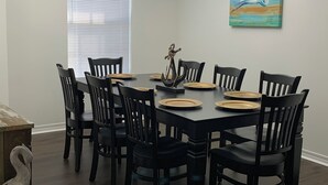 A dining room with a dark wooden table set for six, surrounded by black chairs. A chandelier hangs from the ceiling, and a painting of a bird is on the wall. - Newly Renovated, 1/2 acre home 3 miles from beach (Navarre)
