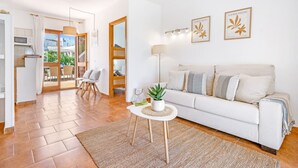 Uma sala de estar moderna com um sofá branco, uma mesinha redonda com uma planta e vista para o exterior através de uma porta de vidro.