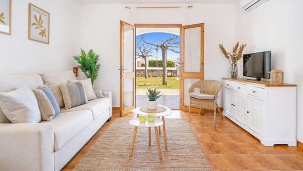 Uma sala de estar com sofá, mesa pequena, televisão e vista para o exterior.