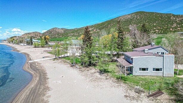 Una propiedad costera con una casa moderna, una playa de arena y un paisaje montañoso al fondo.