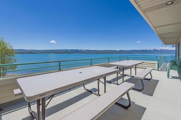 Guests can enjoy scenic views of the water and mountains from this outdoor seating area, featuring picnic tables and benches under a covered section.