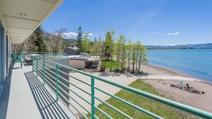 A balcony with a view of a lake, a covered area, and a building in the background. - Bear Lake Paradise | Beach + Boat Ramp (Laketown)