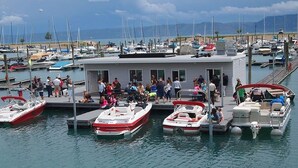 A marina with several boats docked, a covered area with people, and a clear view of the water and distant mountains. - Bear Lake Paradise | Beach + Boat Ramp (Laketown)
