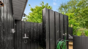 Een houten terras met een zwarte omheining, een douche en een groene tuinslang.