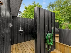 A wooden deck with a black fence, a shower, and a green garden hose.