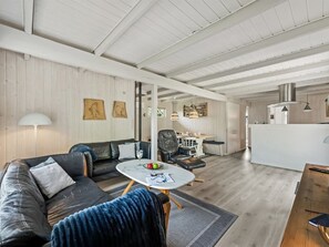 A modern living room with a sofa, a coffee table, and a dining area with a kitchen in the background.