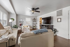 A living room with a sofa, armchair, TV, and ceiling fan.