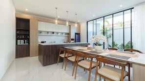 A modern kitchen with a central island, wooden cabinets, and a dining area with a table and chairs. - Swan Villa 4 Seminyak (Seminyak)