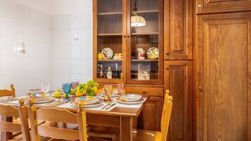 A dining area with a wooden table set for four, surrounded by wooden chairs. A wooden cabinet with glass doors is visible in the background.