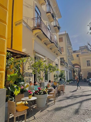 A cobblestone street with outdoor seating at a café, surrounded by yellow buildings with balconies.