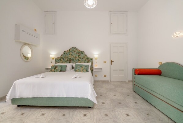 A bedroom with a bed, bedside tables, a mirror, a door, and a green sofa.