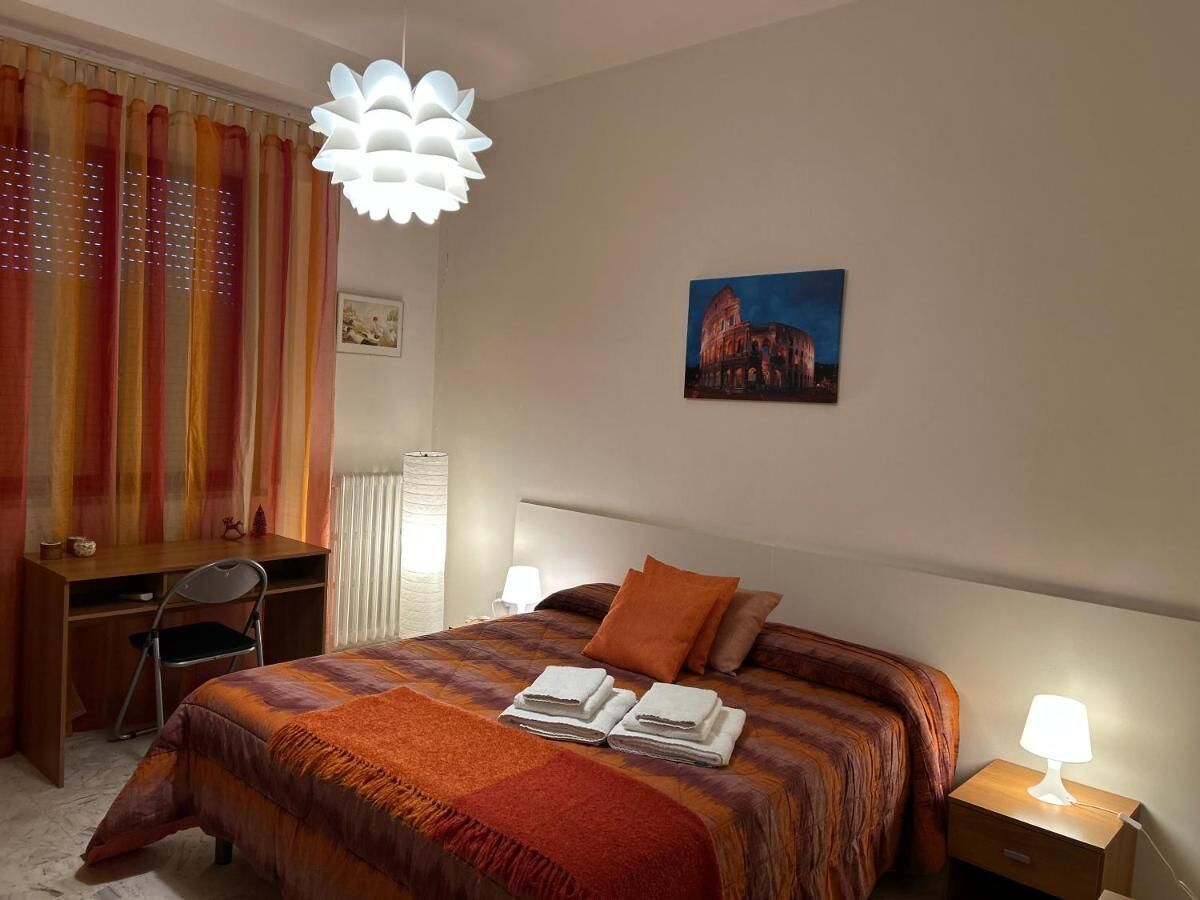 A hotel room with a bed, a desk, a chair, a lamp, and a picture on the wall.