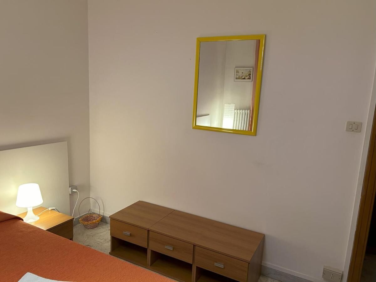 Quarto com penteadeira de madeira, mesa de cabeceira com abajur e espelho com moldura amarela.
