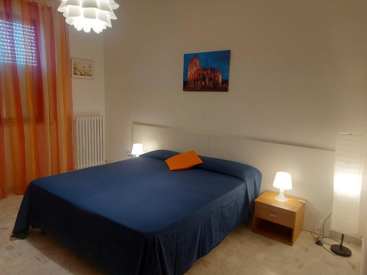 Een slaapkamer met een bed, nachtkastje, lamp, foto aan de muur en een raam met gordijnen.