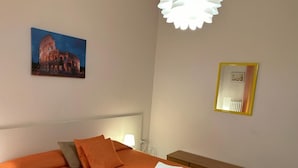 A hotel room with a large bed, a bench, a bedside table, a lamp, a framed picture, and a ceiling light fixture. - Accogliente Appartamento per Famiglie al Centro (Lavello)