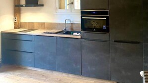 Une cuisine moderne avec des meubles de couleur sombre, un plan de travail en bois, un four encastré et une fenêtre au-dessus de l’évier.
