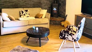 Un salon avec un mur en pierre, un canapé, une table basse ronde, un fauteuil à motifs de vaches, un téléviseur à écran plat et une cheminée.