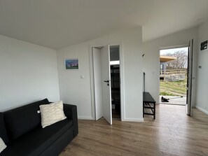 A room with a black sofa, a white door leading to a balcony, and a wooden floor. - Cozy tiny house in nature - Holiday home D (Sejerø)