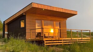 Una cabaña moderna de madera con ventanas amplias, un balcón y entorno cubierto de césped.