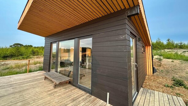 Una cabaña moderna con techo inclinado, ventanas de vidrio amplias y una terraza de madera.