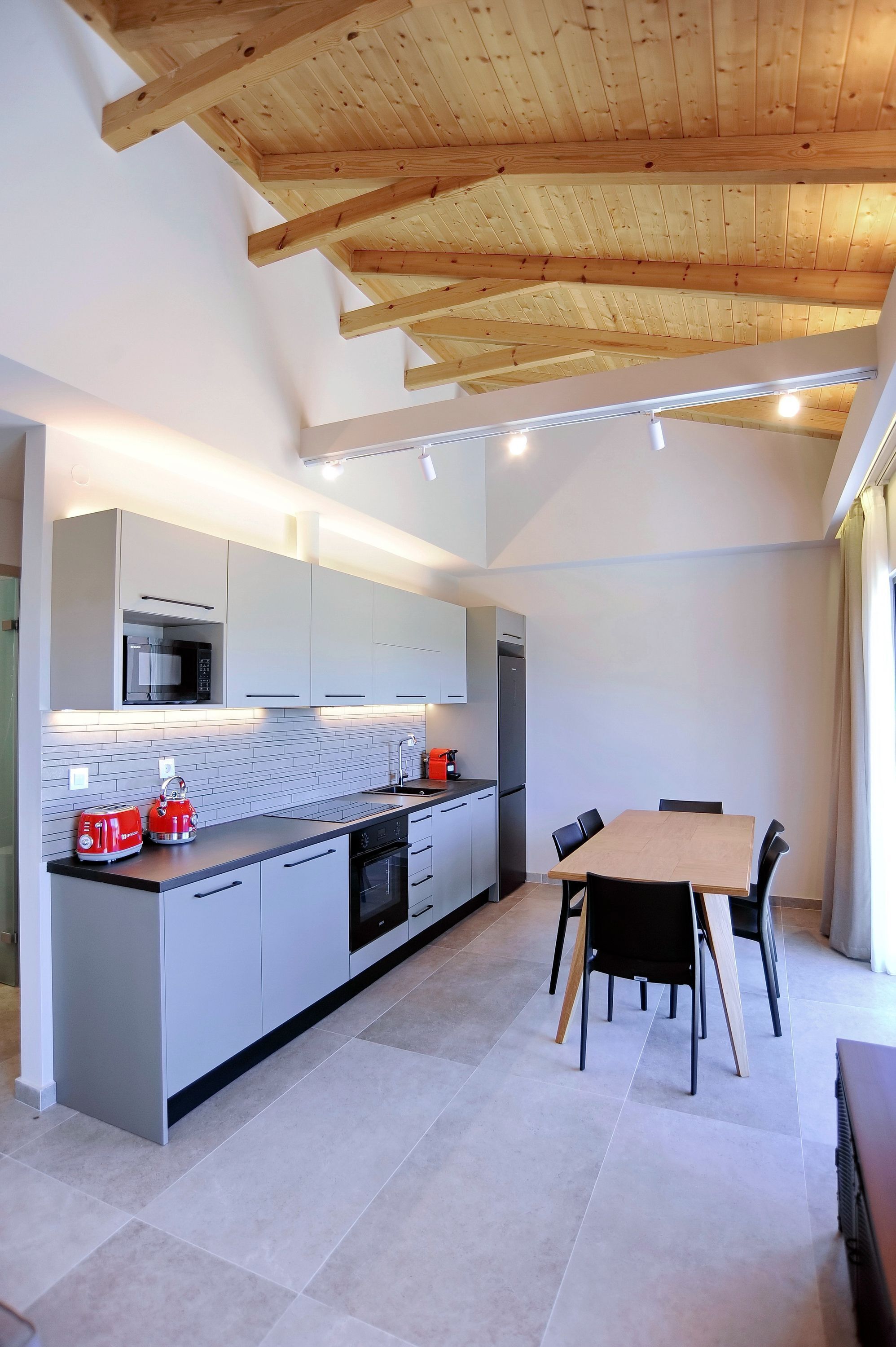 A modern kitchen with white cabinets, a wooden ceiling, and a dining area with a table and chairs.