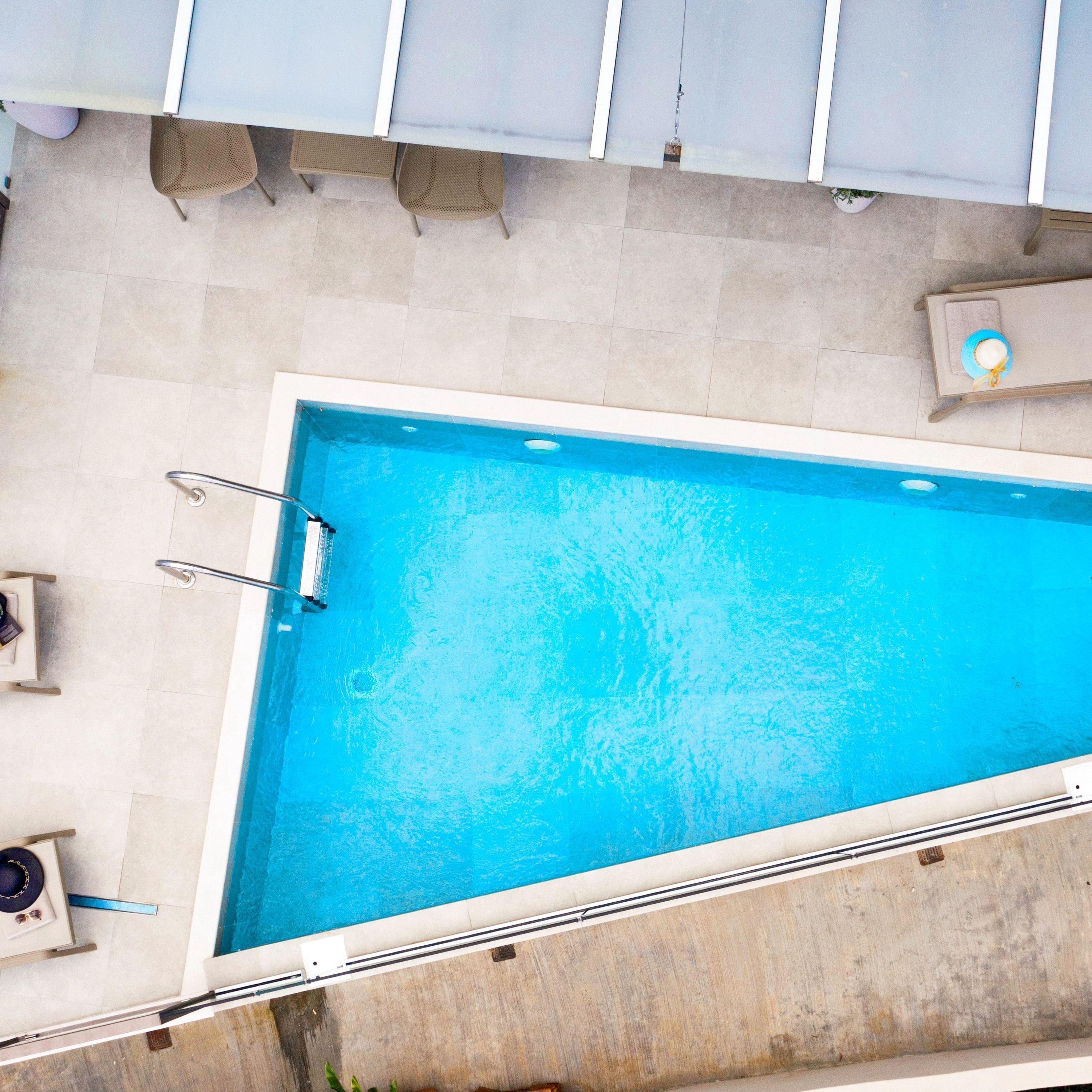 A rectangular swimming pool with a metal ladder on one side, surrounded by light-colored tiled flooring.